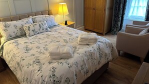 Ett hotellrum med en säng, ett nattduksbord med en lampa, en garderob, en stol och ett fönster med gardiner.