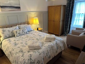Hotelkamer met een bed, nachtkastje met lamp, kledingkast, stoel en raam met gordijnen.