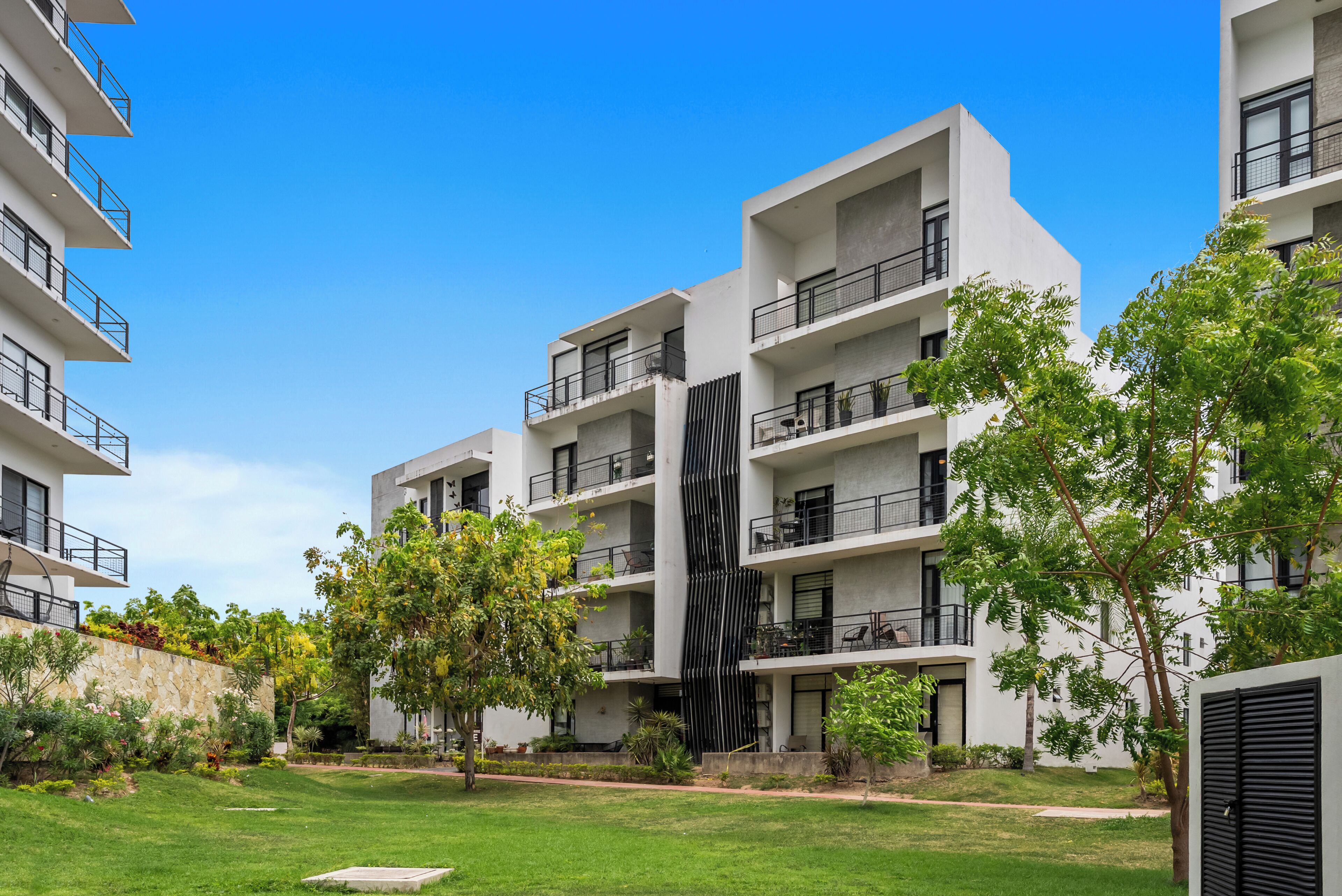 A modern multi-story residential building with balconies, a central vertical feature, and surrounding greenery.