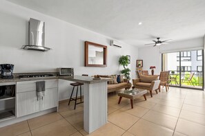 Eine moderne Küche mit einer zentralen Kochinsel, ein Essbereich mit einer Couch und Sesseln sowie ein Balkon mit Blick.