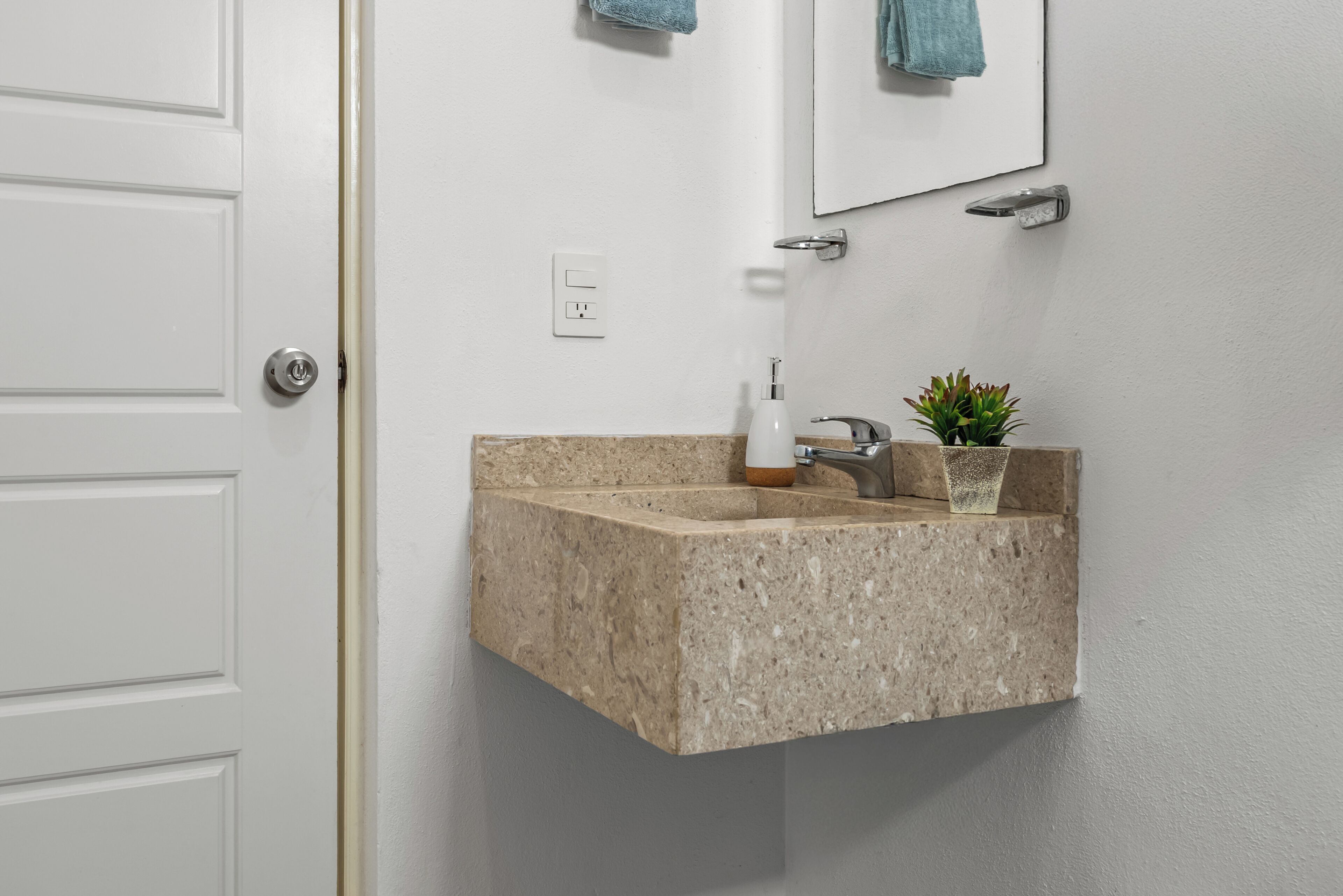A bathroom with a granite countertop sink, a mirror, a towel rack, and a small potted plant.