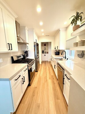 Une cuisine moderne avec des meubles blancs, des appareils en acier inoxydable et un plancher en bois.