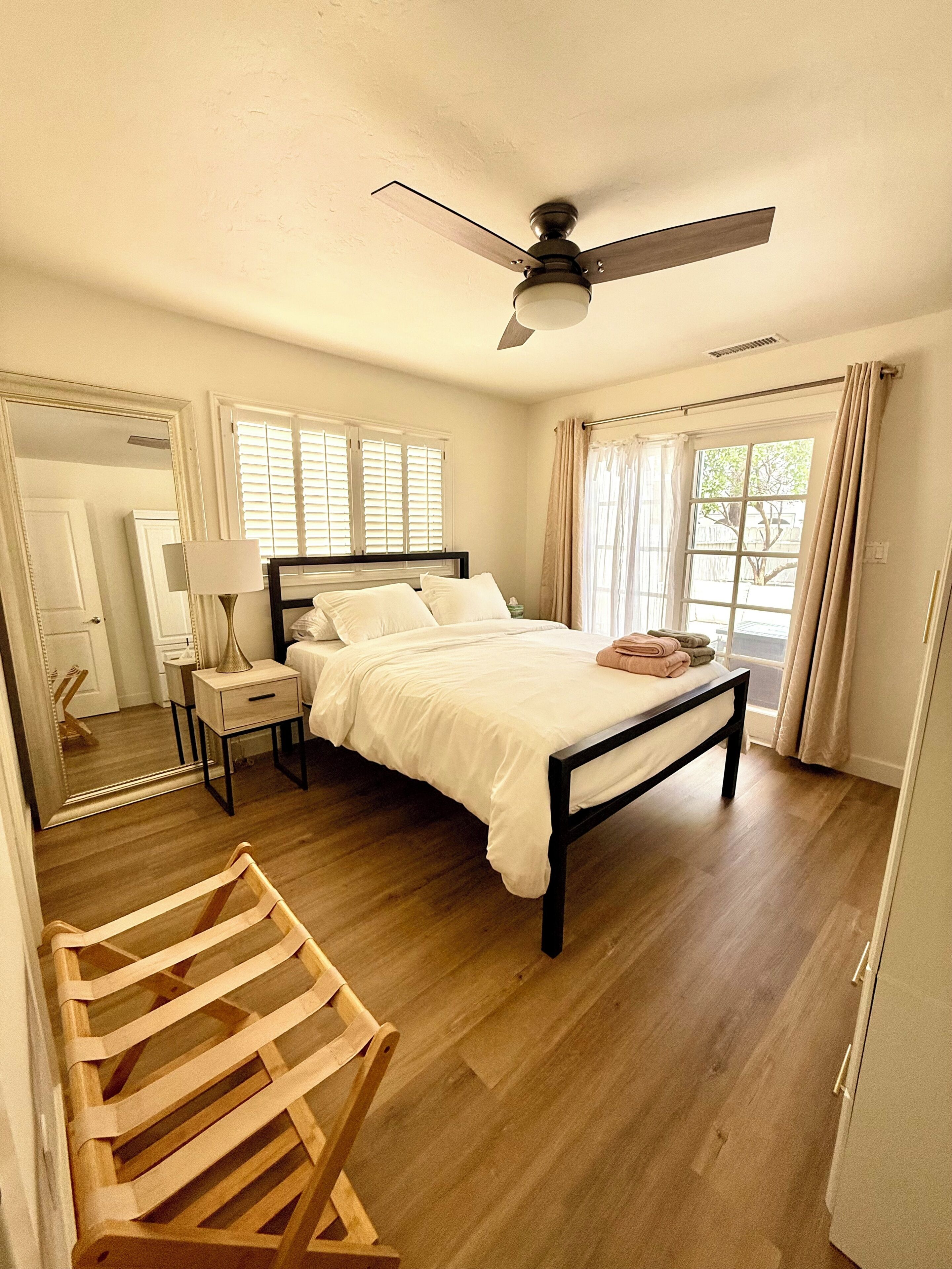 Une chambre à coucher comprenant un lit, une table de chevet, une lampe, un ventilateur de plafond et une chaise en bois.