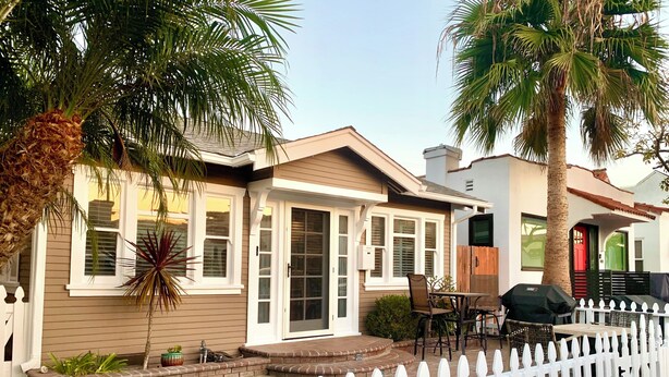 Ein Wohnhaus mit weißem Zaun, einer Veranda und einer Terrasse mit Gartenmöbeln.