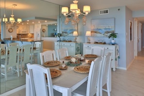 A dining area with a large table, white chairs, and a chandelier. - Serene Saltwater Sanctuary | Inlet #607 (New Smyrna Beach)