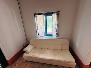 A corner room with a beige sofa, a window with patterned curtains, and a view of greenery outside. - Creekvista Vista y Encanto del Charco (Cocorná)
