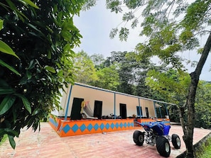 A building with a tiled floor, a blue and orange exterior, and a blue vehicle parked in front. - Creekvista Vista y Encanto del Charco (Cocorná)