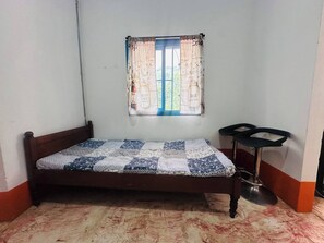 Ein kleines Zimmer mit einem Einzelbett, einem Fenster mit gemusterten Vorhängen und einem kleinen Tisch.