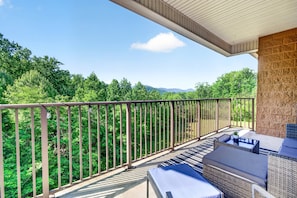 A balcony with outdoor furniture, a stone wall, and a view of dense green trees. - Venus 145 2 Bedroom Condo (Gatlinburg)