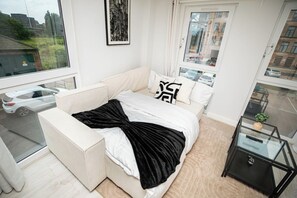 A modern bedroom with a bed, a glass table, and a view of the outside. - Luxury 2 Bed Apt at Victoria Riverside | Parking (Leeds)