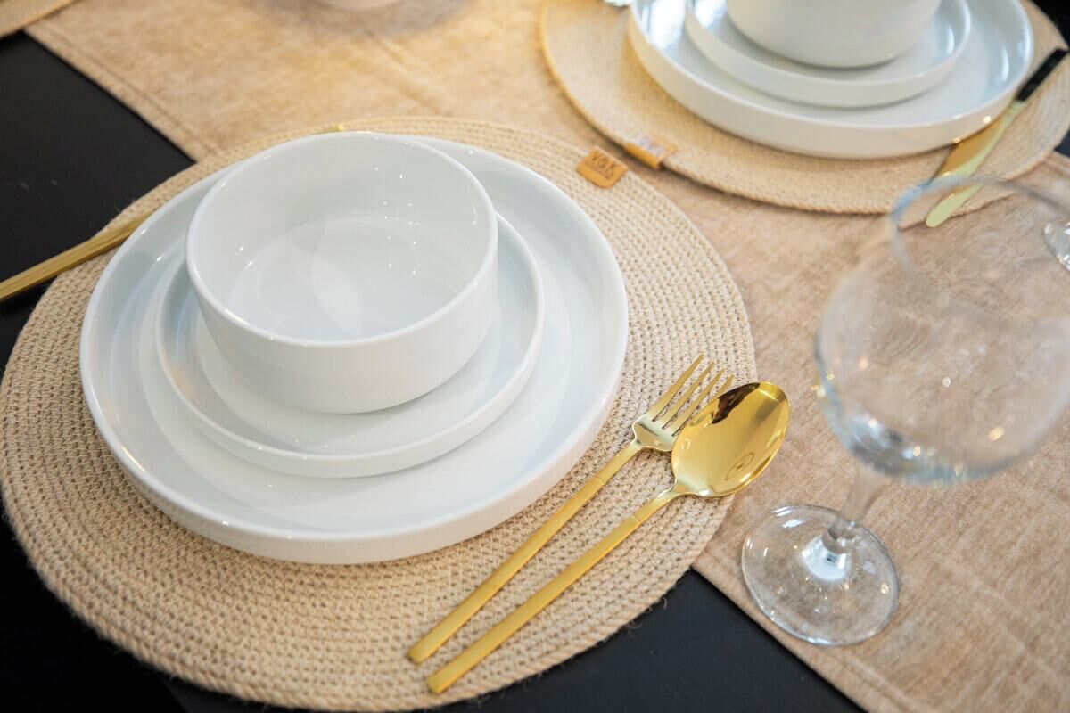 A table set with white plates, gold cutlery, and a wine glass.
