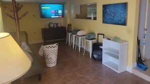 Ein Wohnzimmer mit Fernseher, einem Gemälde, einer Lampe, einem Mülleimer und einem Koffer.