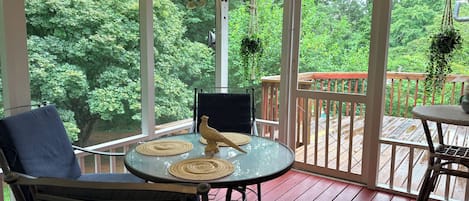A covered outdoor seating area with a table and chairs, overlooking a wooden deck and lush greenery.
