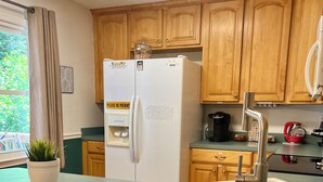Una cocina con armarios de madera, un refrigerador blanco, un lavamanos de acero inoxidable y una planta en maceta.