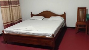 Een enkel bed met houten frame, een groene tafel met een stoel, en een vloer met een rood tapijt.