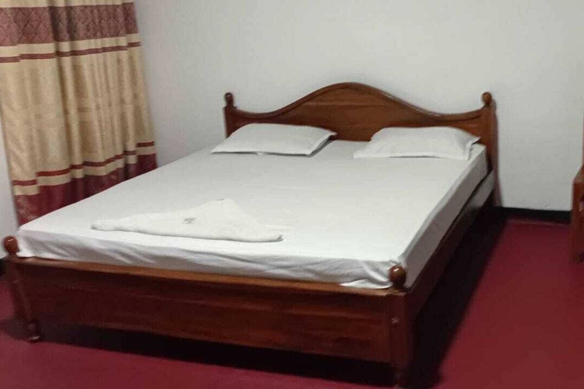 A single bed with a wooden frame, a green table with a chair, and a red carpeted floor.