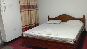 Een enkel bed met een houten hoofdbord, witte lakens en een rode vloerbedekking.