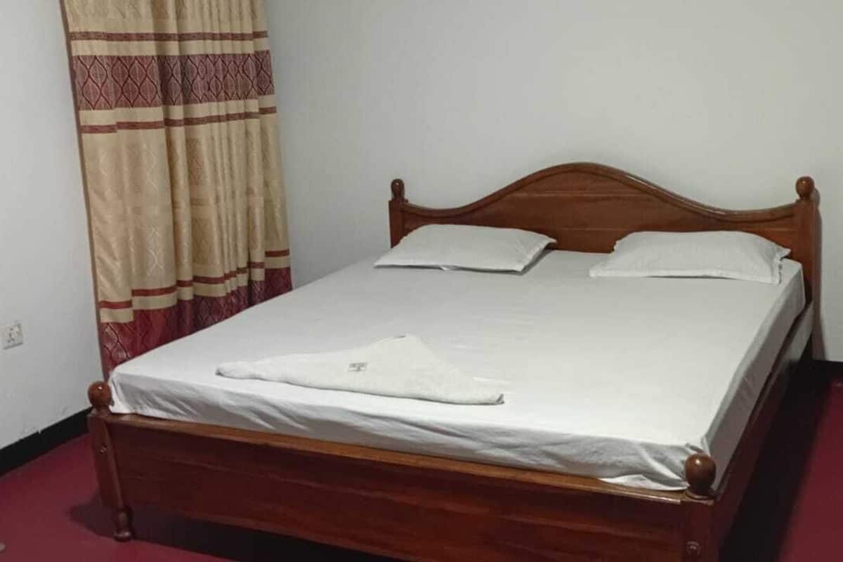 A single bed with a wooden headboard, white linens, and a red carpeted floor.