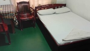 Een kamer met een enkel bed, een houten stoel, een tafel met een geruit tafelkleed en een groene vloer.