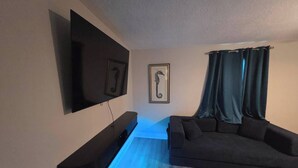 Uma sala de estar moderna com televisão de tela plana na parede, um sofá escuro e uma obra de arte com um cavalo-marinho emoldurado.