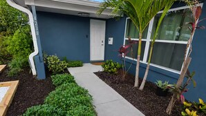 Uma casa com fachada azul, porta branca e caminho de concreto que leva à entrada.