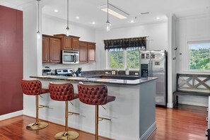 Una cocina con una isla central, taburetes de bar, armarios de madera, un microondas, un refrigerador y una ventana con vistas.