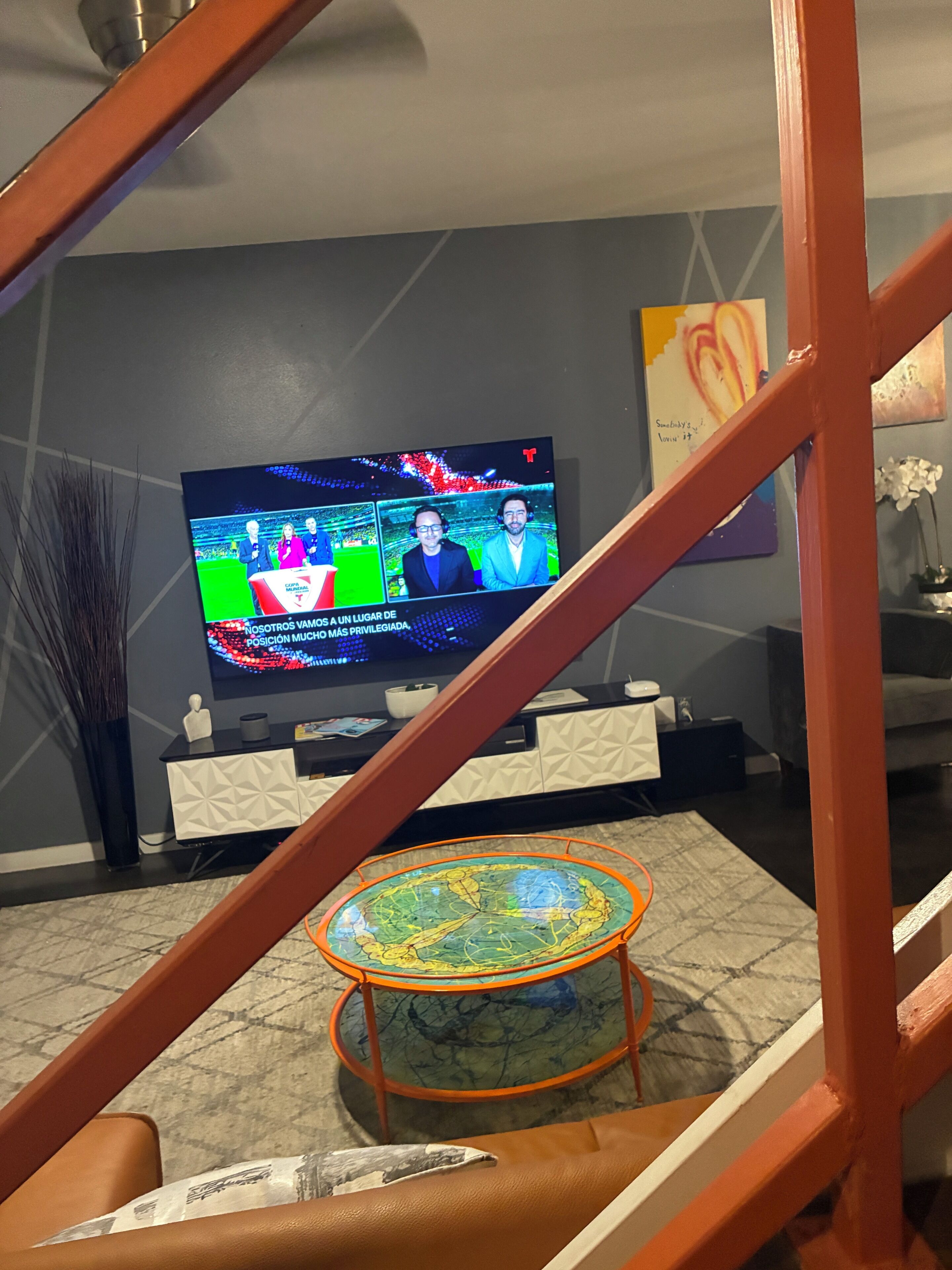 Un soggiorno con una televisione che mostra una trasmissione televisiva, un tavolino globo e una scala.