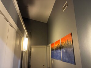 Un couloir avec une porte, un luminaire et un tableau accroché au mur.