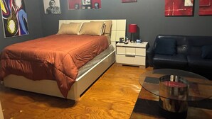A modern bedroom with a bed, bedside table, lamp, and a blue sofa.