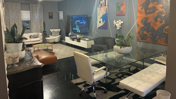 A modern living room with a glass dining table, leather sofas, a large flat-screen TV, and abstract art on the walls.