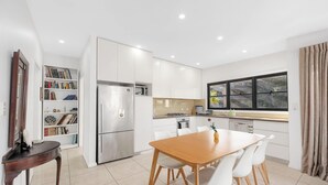 A modern kitchen with white cabinetry, a stainless steel refrigerator, a dining table with chairs, and a window with curtains. - MetaWiseBnB Bondi Junction Penthouse Style (Bondi Junction)