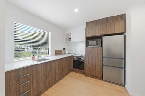 Une cuisine moderne avec des meubles en bois, un réfrigérateur en acier inoxydable, un four à micro-ondes et une fenêtre avec des stores.