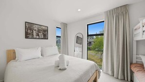 Hotellihuone, jossa on suuri sänky, ikkuna, jossa on verhot, kerrossänky ja seinällä oleva kehystetty kuva.
