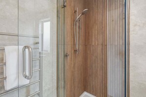 Une salle de bain moderne dotée d’une douche à parois de verre, d’un mur recouvert de panneaux en bois et d’une porte en verre avec un porte-serviettes.