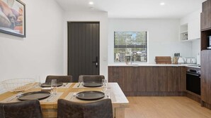 Moderni keittiö, jossa on ruokailutila, puukaapit, ikkuna, jossa on sälekaihtimet, ja ovi.