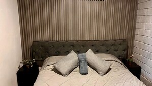 Ein Bett mit einer gesteppten Kopfteil, einer neutralen Tagesdecke und zwei Kissen.