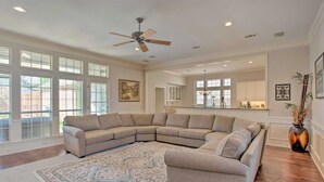 A spacious living room with a large L-shaped sectional sofa, a patterned rug, and a ceiling fan. - Private Pool & Hot Tub Suburban Retreat (Plano)