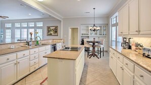 A spacious kitchen with white cabinetry, a granite countertop, a central island, and a dining area with a chandelier. - Private Pool & Hot Tub Suburban Retreat (Plano)