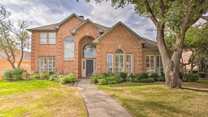 A two-story brick house with a front entrance, a covered porch, and a pathway leading to the door. - Private Pool & Hot Tub Suburban Retreat (Plano)