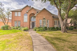 A two-story brick house with a front entrance, a covered porch, and a pathway leading to the door. - 4-BR Upscale Suburban Home with Private Pool (Plano)