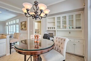 A dining area with a round glass table, a tufted chair, a chandelier, and white cabinetry. - 4-BR Upscale Suburban Home with Private Pool (Plano)