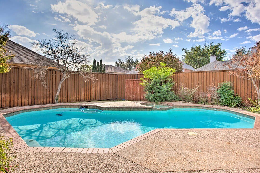 A backyard with a swimming pool, wooden fence, and trees.