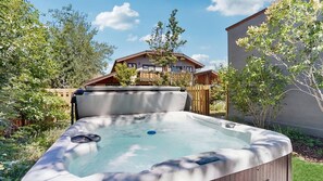 A hot tub in a garden with a wooden fence and a building in the background. - Spacious home near town w/ private hot tub- next to trails & river (Ketchum)