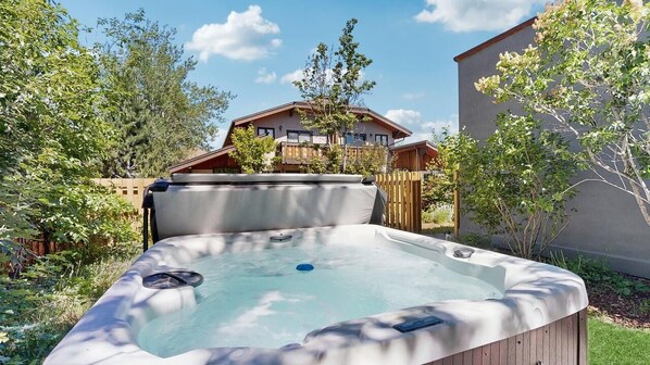 Ein Whirlpool in einem Garten mit Holzzaun und einem Gebäude im Hintergrund.
