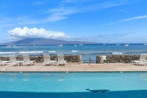 Ein Pool mit Liegestühlen, einer Steinmauer und Segelbooten auf dem Wasser.