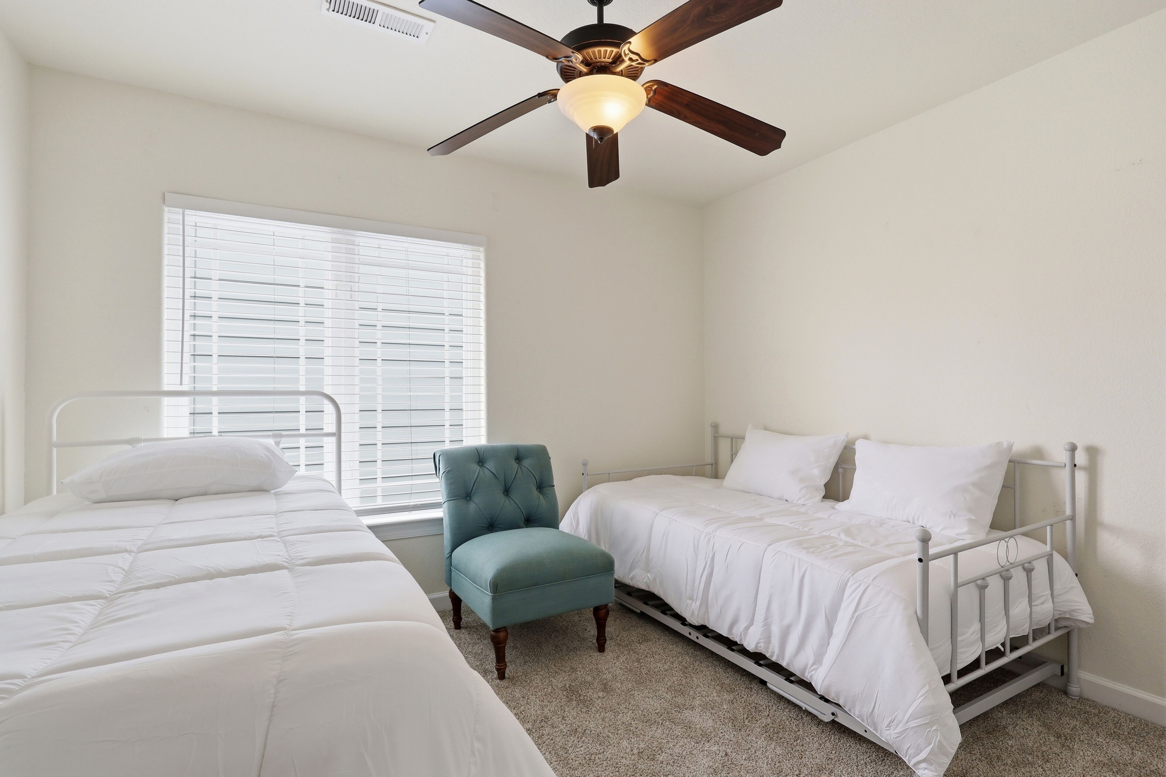 A bedroom with two beds, a ceiling fan, a window with blinds, and a chair.