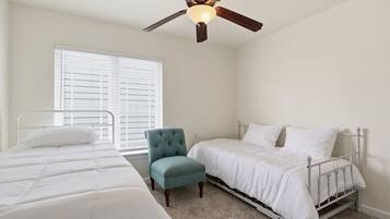 A bedroom with two beds, a ceiling fan, a window with blinds, and a chair.