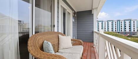 A balcony with a wicker sofa, white curtains, and a view of a building with multiple windows.
