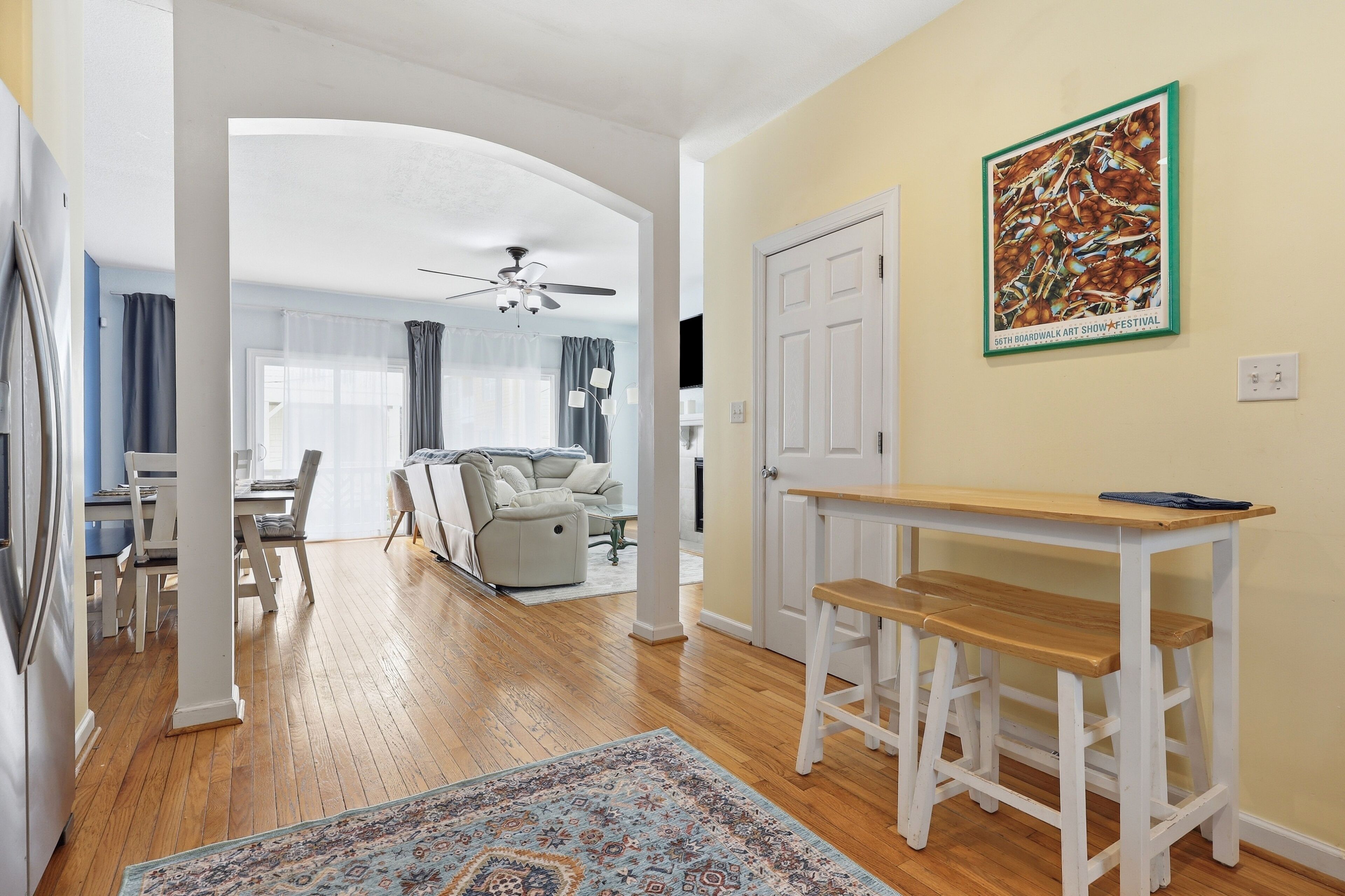 A spacious living area with a wooden floor, a dining table, a sofa, and a ceiling fan.