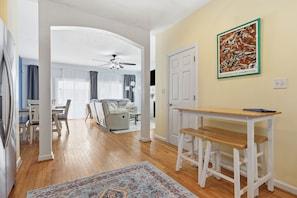 A spacious living area with a wooden floor, a dining table, a sofa, and a ceiling fan.
